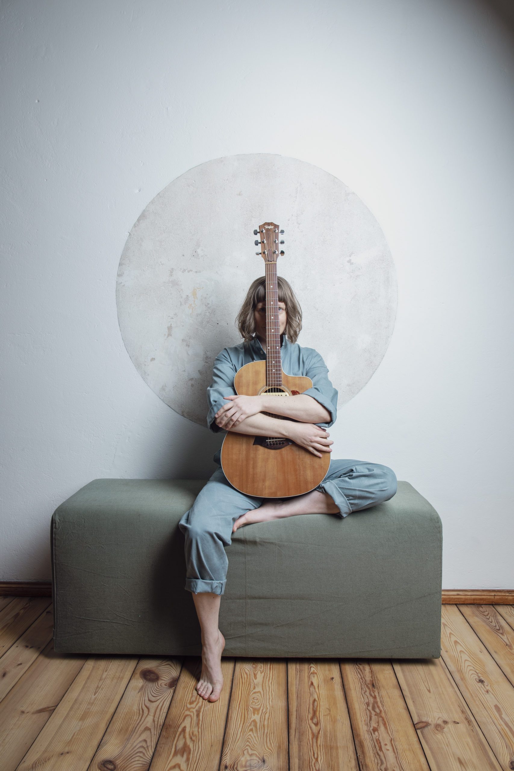 Ein Portrait der Musikerin Teresa Bergman. Sie sitzt auf einem Hocker und hält eine Gitarre vor sich