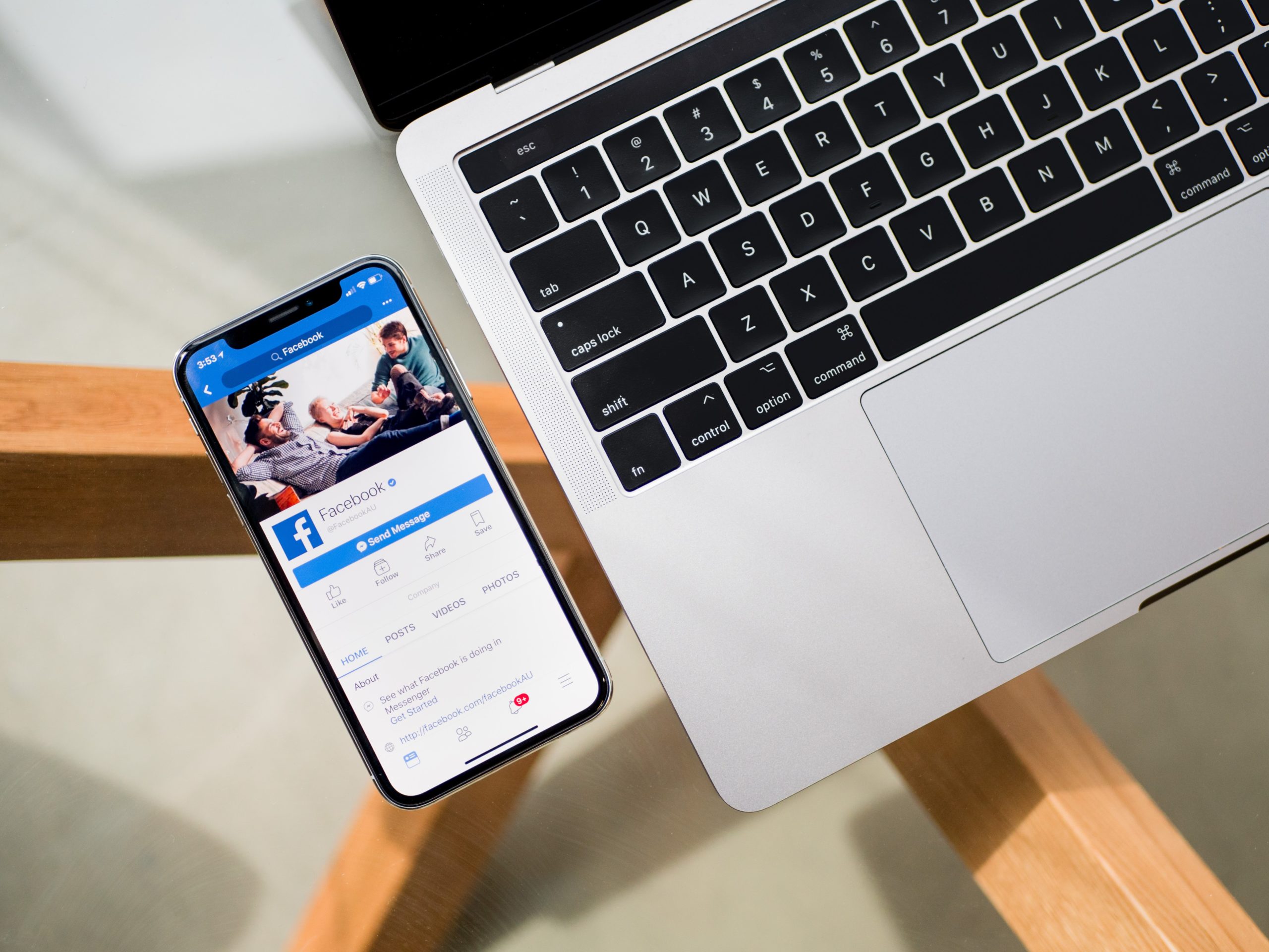 Neben einem Laptop liegt ein Handy. Darauf zu sehen ist ein geöffnetes Facebook-Profil